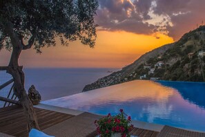 Un espace aménagé au bord de la piscine, offrant une vue sur la mer et le coucher du soleil.
