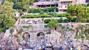 A coastal building with multiple balconies, a stone staircase, and a boat in the water. - SELENE - Eight Bedroom Villa, Sleeps 16 (Ravello)