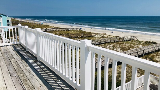 A wooden deck with white railings overlooking a beach with a wooden boardwalk and a small structure in the distance. - Oceanfront 9 bdrms with pool and hot tub (Carolina Beach)