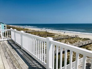 A wooden deck with white railings overlooking a beach with a wooden boardwalk and a small structure in the distance. - Oceanfront 9 bdrms with pool and hot tub (Carolina Beach)
