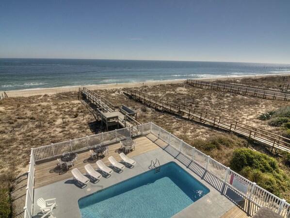 A pool area with lounge chairs and a view of the beach.