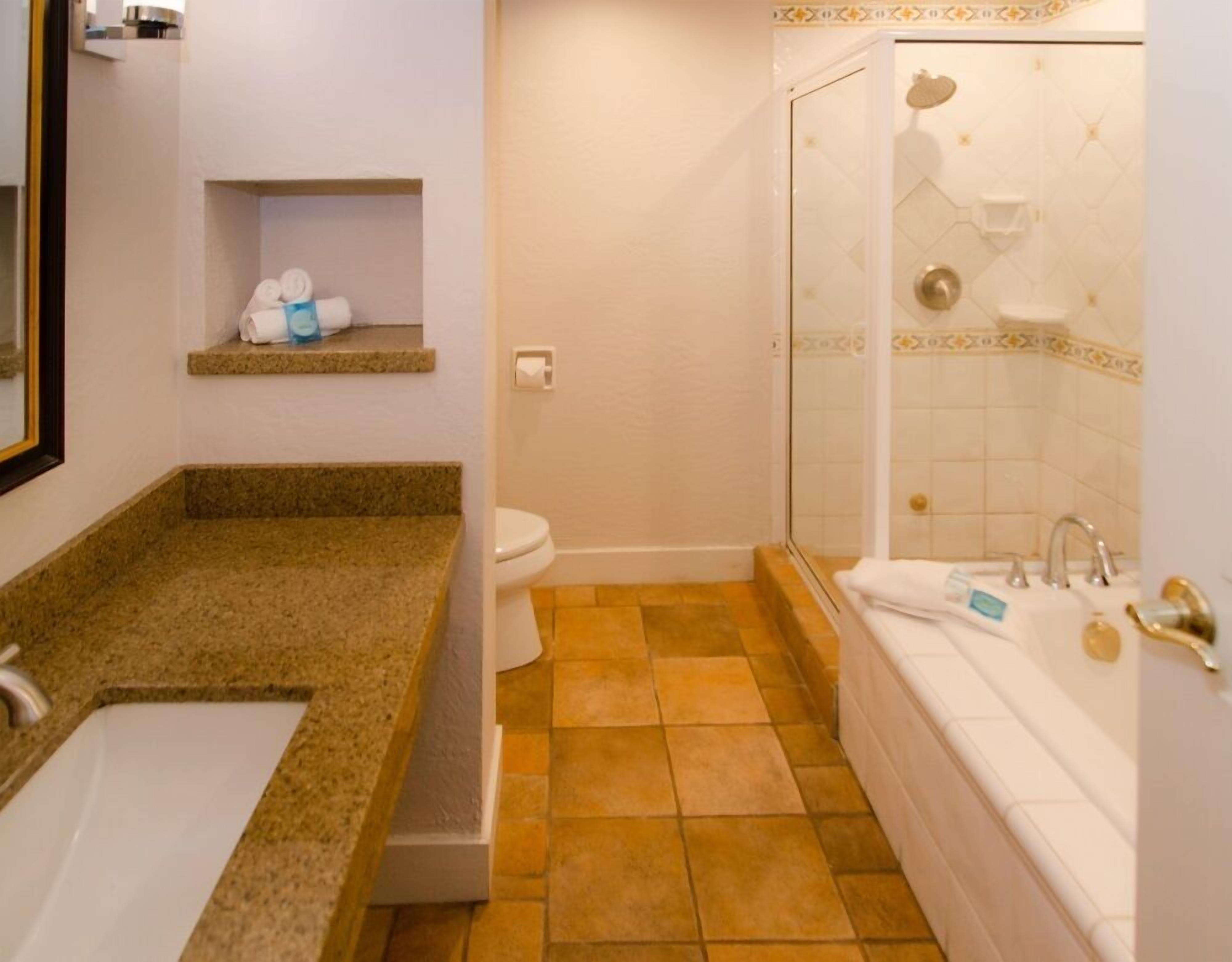 Une salle de bain comprenant un lavabo avec un plan de toilette en granit, des toilettes, une baignoire et un espace douche.