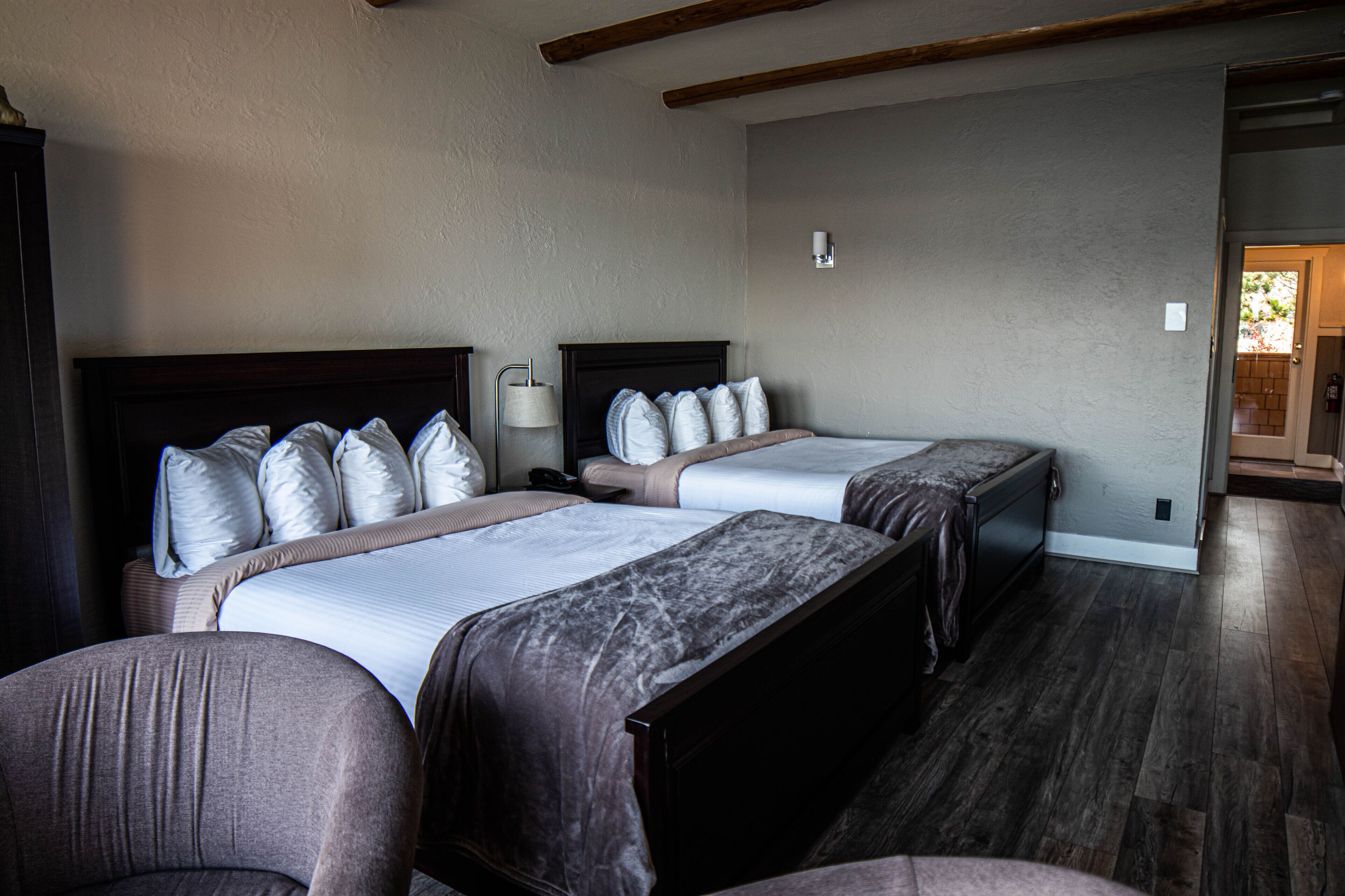A hotel room with two beds, a wooden floor, and a door leading to another room.