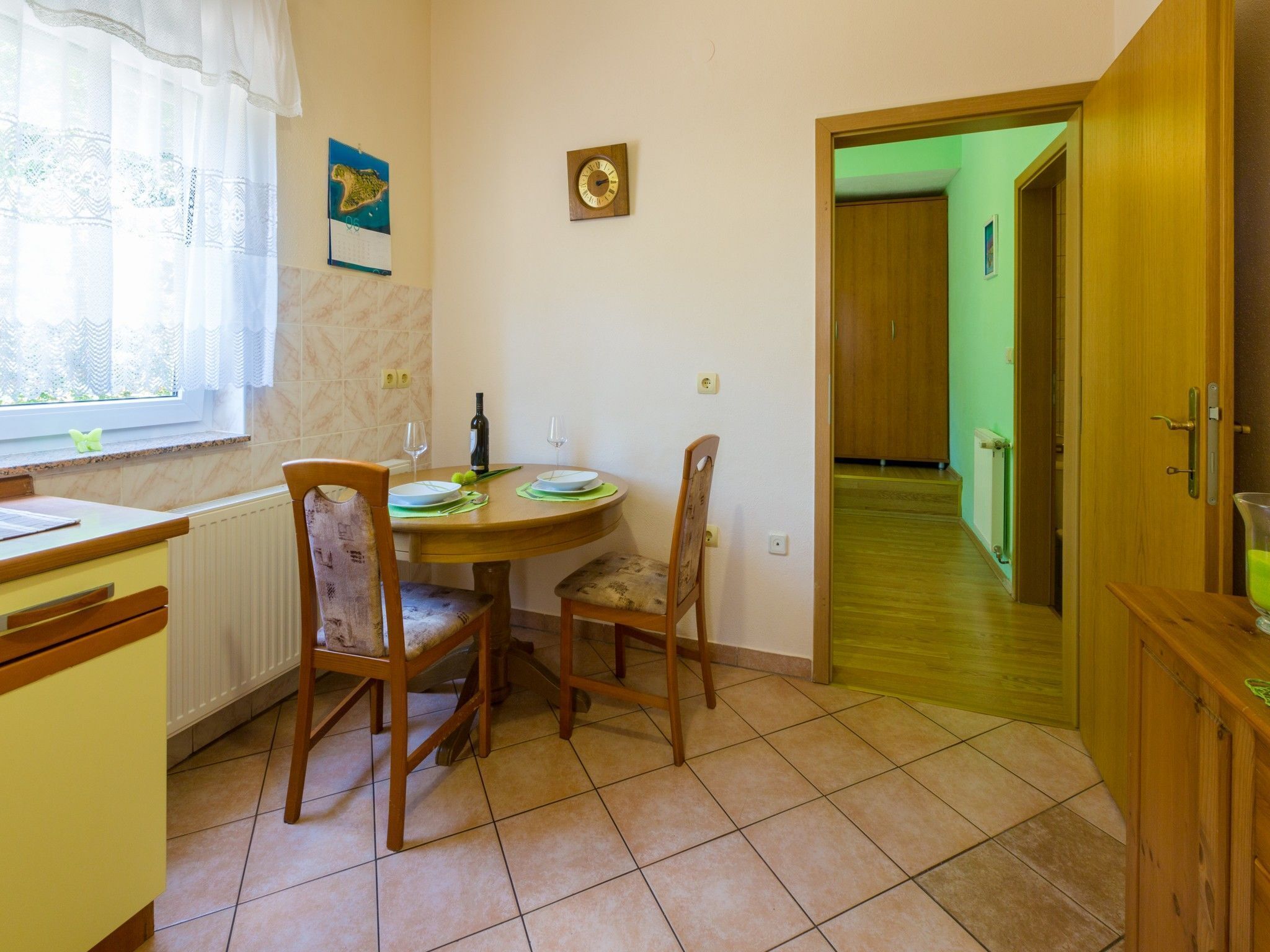 Un comedor con una mesa redonda, dos sillas, una botella de vino y un reloj en la pared.