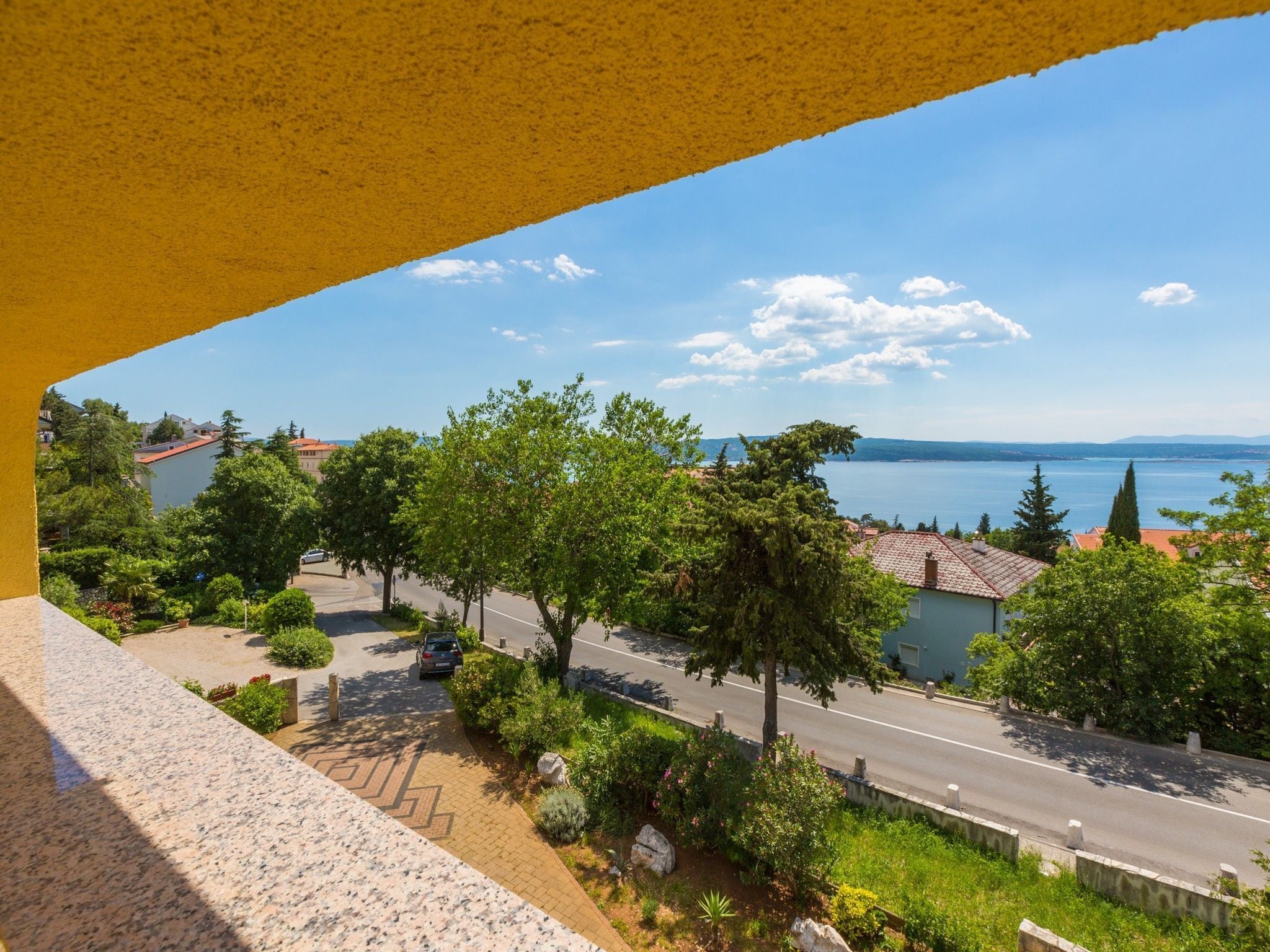 Ein Balkon mit Blick auf eine Wohnstraße, Bäume und ein Gewässer.