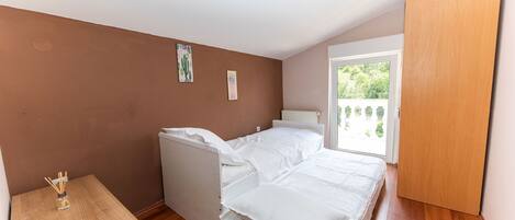 A bedroom with a bed, a small wooden table, and a window with a view of greenery.