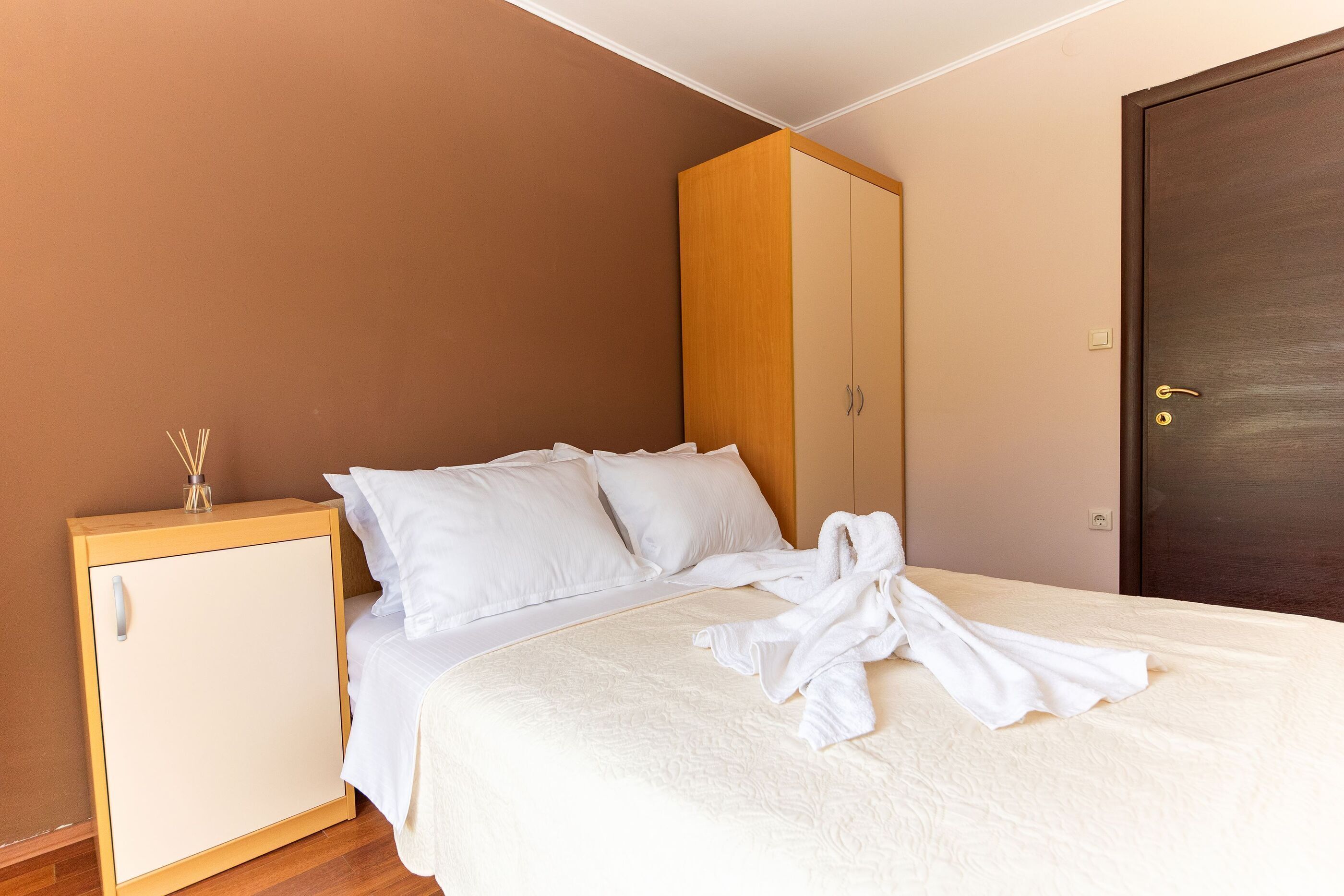 A neatly made bed with white bedding, a wooden wardrobe, and a closed door in a hotel room.