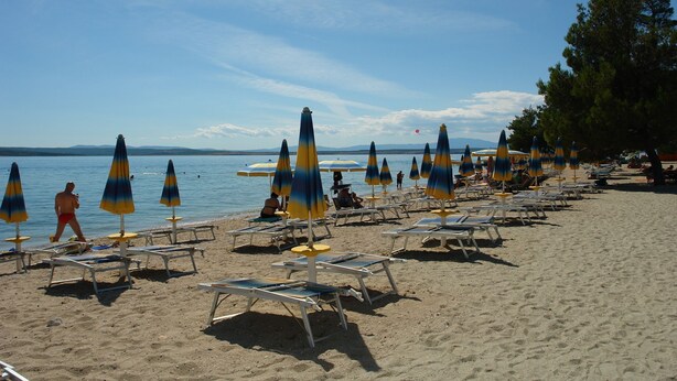 Ein Strand mit Reihen von Liegestühlen und Sonnenschirmen, einem klaren Himmel und ruhiger See.