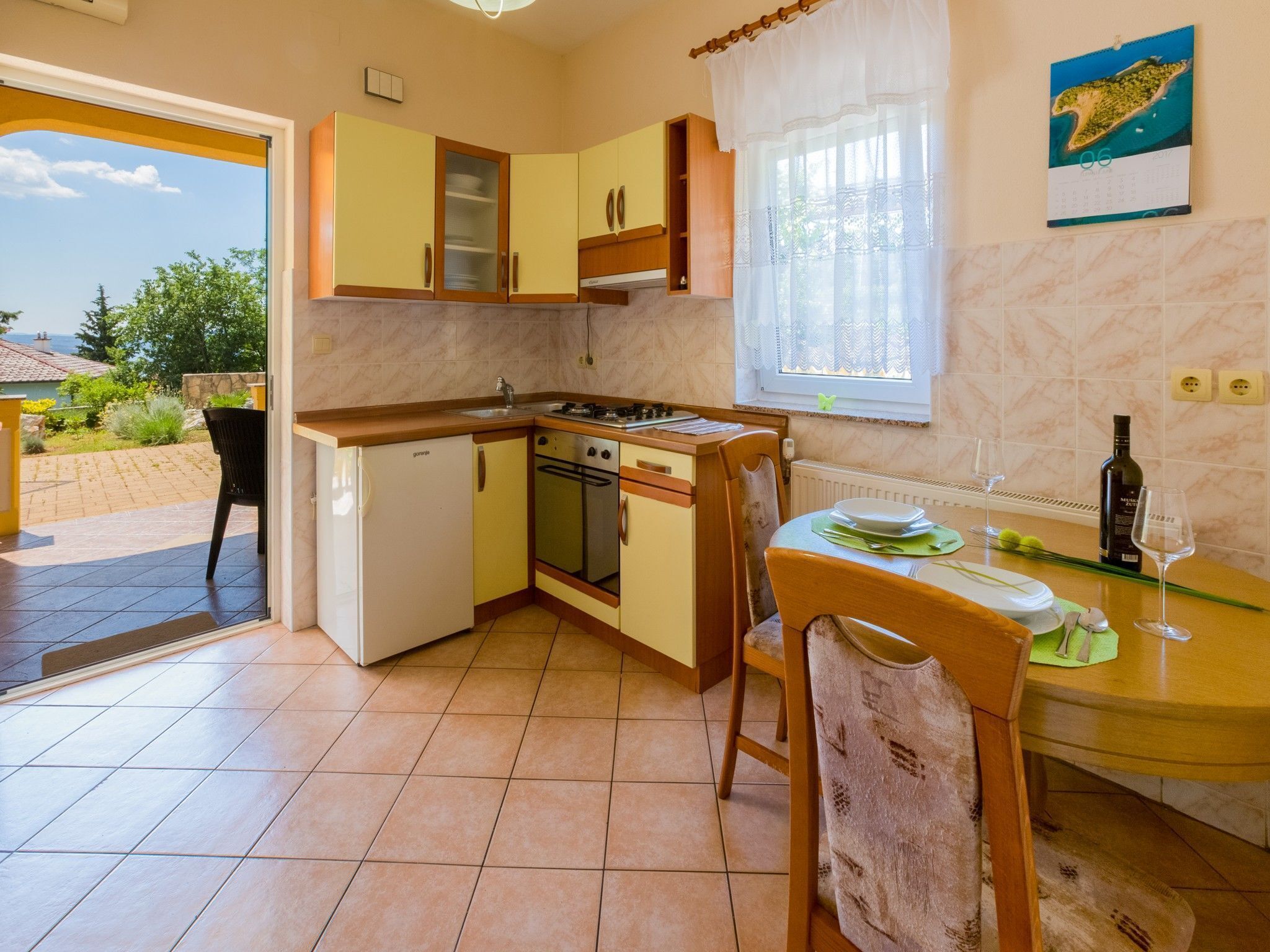 A compact kitchen with a dining area, a refrigerator, an oven, and a window with a calendar.