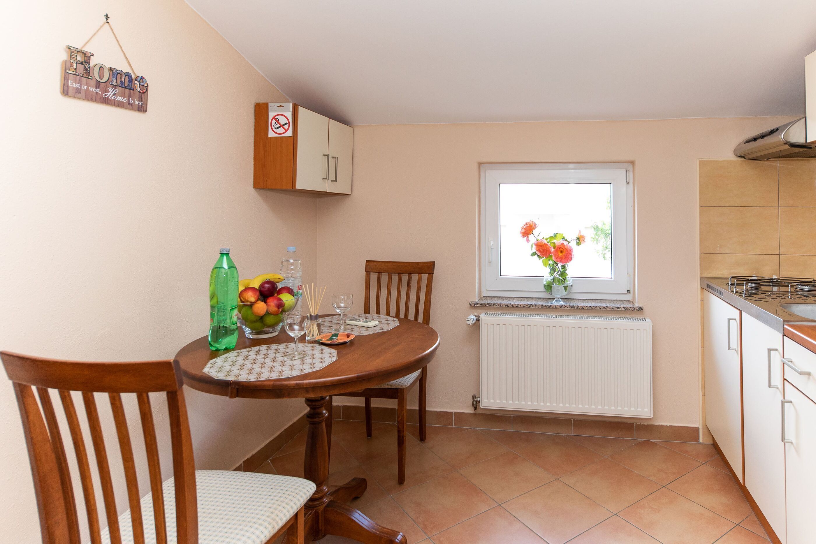 A small kitchen with a dining table set for two, a window with flowers, and a sign on the wall.