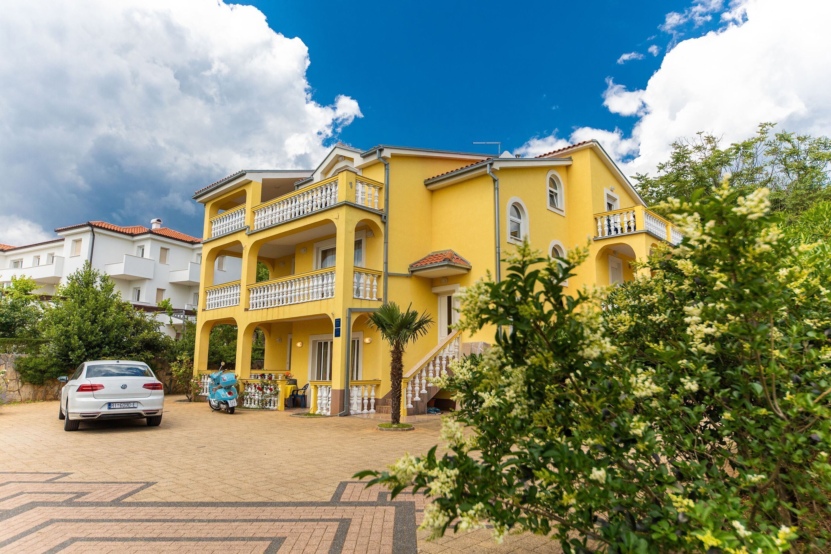Un bâtiment jaune avec un balcon, une voiture et une moto garées devant.