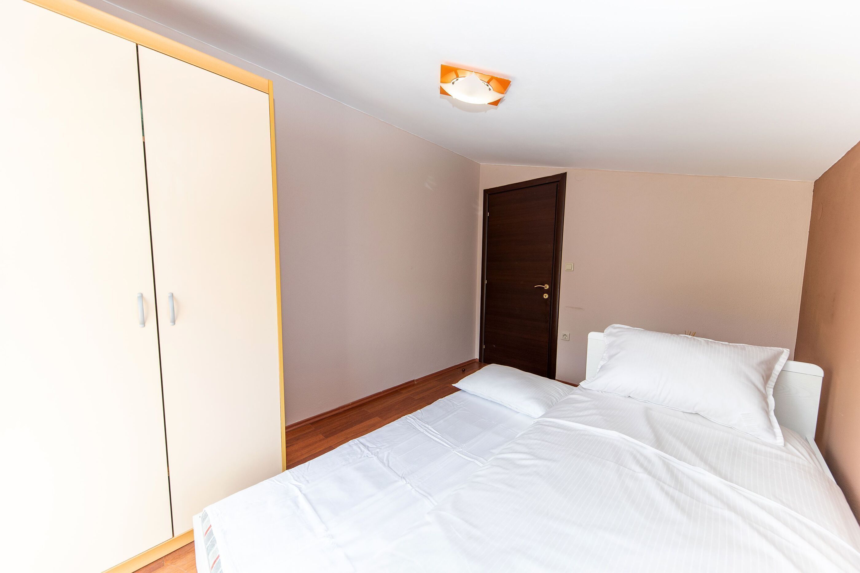 Une chambre à coucher avec un lit, du linge de lit blanc, une armoire et une porte.