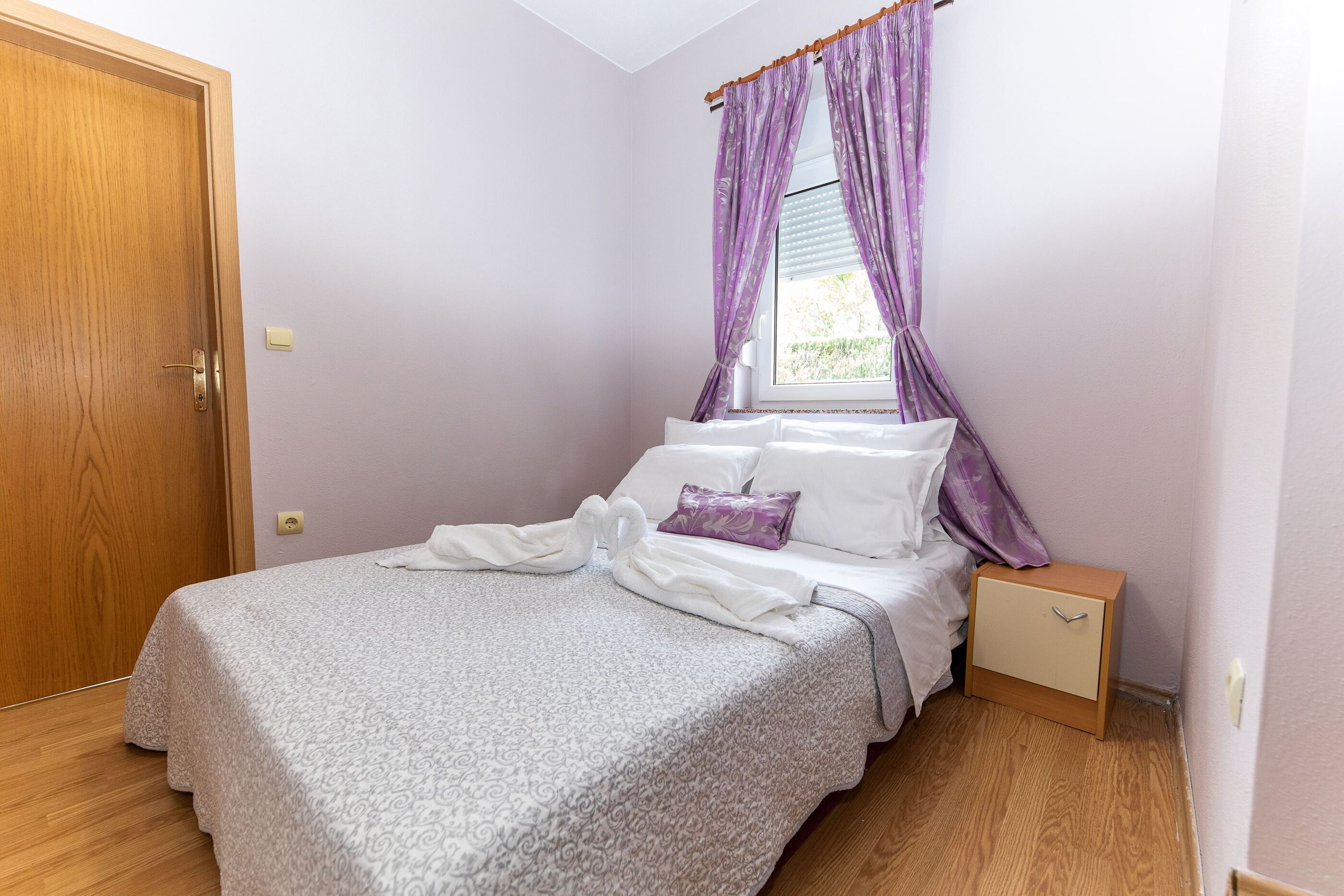 Une chambre à coucher avec un lit, une table de chevet, une porte en bois et des rideaux violets.