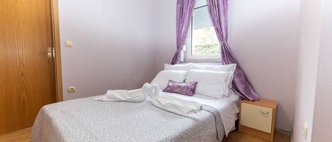 Une chambre à coucher avec un lit, une table de chevet, une porte en bois et des rideaux violets.