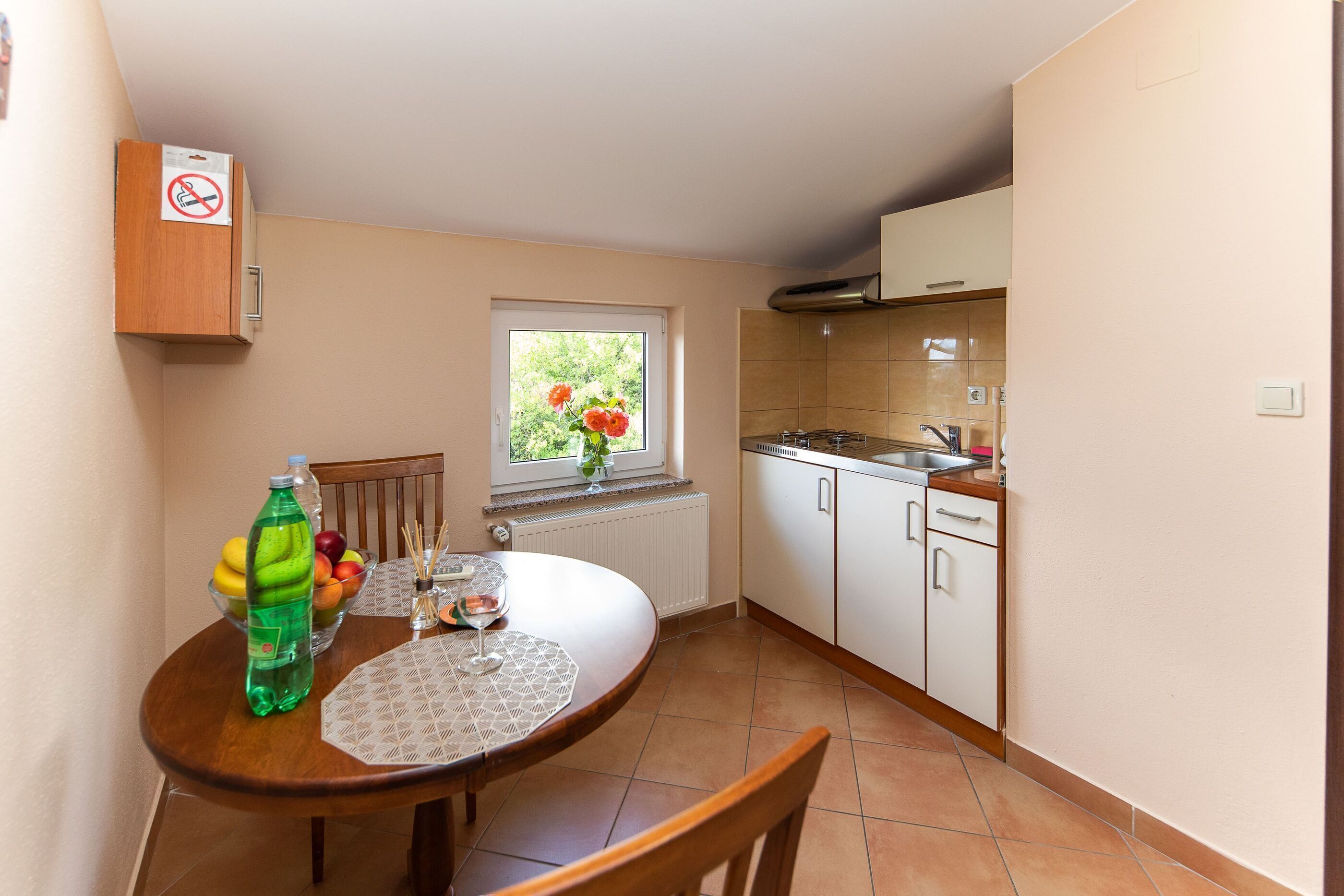 A compact kitchen with a dining area, a window with a view of greenery, and a bottle of soda on the table.