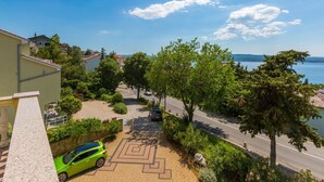 Ein Wohngebiet mit befestigter Auffahrt, einem grünen Auto, das am Straßenrand geparkt ist, und Blick auf das Meer im Hintergrund.