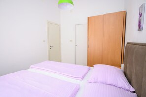 A room with two beds, a wooden wardrobe, and a green pendant light. - Apartments Franco (Selce)