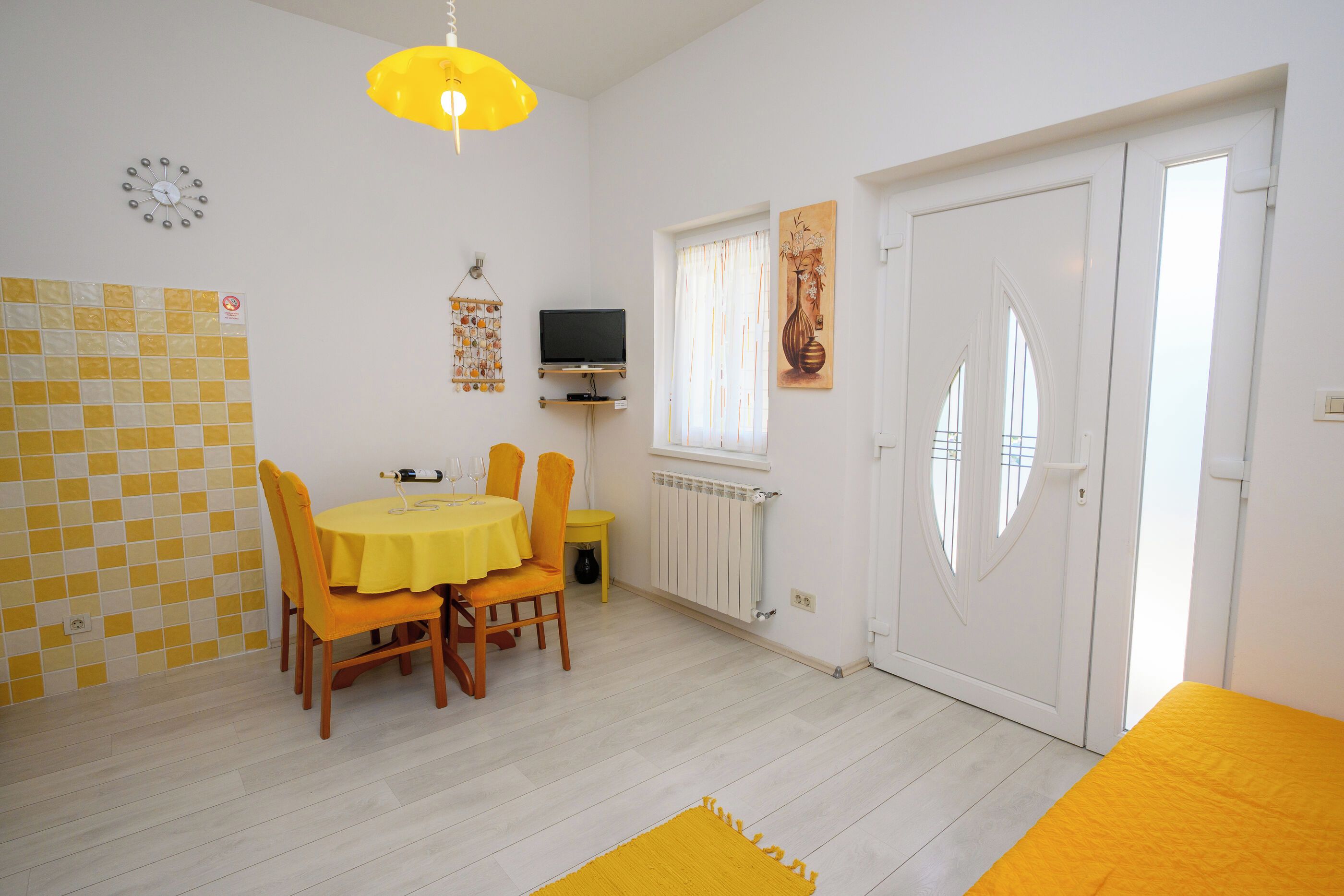 A dining area with a table and chairs, a television on a stand, a radiator, and a door with a window.