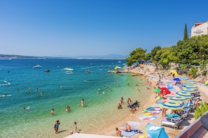 A beach with clear waters, umbrellas, and people swimming.