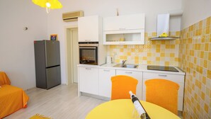 Cozinha compacta com geladeira, forno e uma mesa amarela com uma garrafa.
