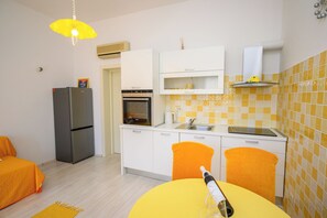 A compact kitchen with a refrigerator, oven, and a yellow table with a bottle.