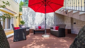 An outdoor patio with wicker furniture, a red umbrella, and a stone wall backdrop. - Apartments Franco (Selce)