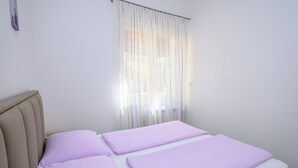 A single bed with a headboard, a window with sheer curtains, and a plain white wall. - Apartments Franco (Selce)