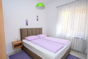 A bedroom with a bed, a nightstand, a lamp, and a window with curtains.
