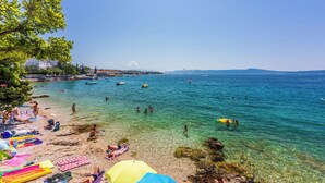 A beach with clear water, people swimming, and colorful umbrellas. - Apartments Franco (Selce)