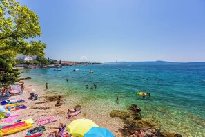 A beach with clear water, people swimming, and colorful umbrellas. - Apartments Franco (Selce)
