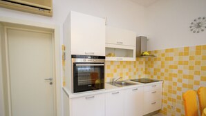 A compact kitchen with white cabinets, a built-in oven, a sink, and a yellow-tiled backsplash. - Apartments Franco (Selce)