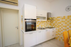 A compact kitchen with white cabinets, a built-in oven, a sink, and a yellow-tiled backsplash. - Apartments Franco (Selce)