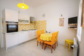 A compact kitchen with a built-in oven, a sink, and a dining area with a yellow table and chairs. - Apartments Franco (Selce)