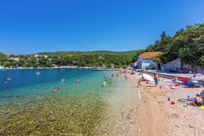 A beach with clear water, people swimming and sunbathing, and buildings in the background. - Apartments Franco (Selce)