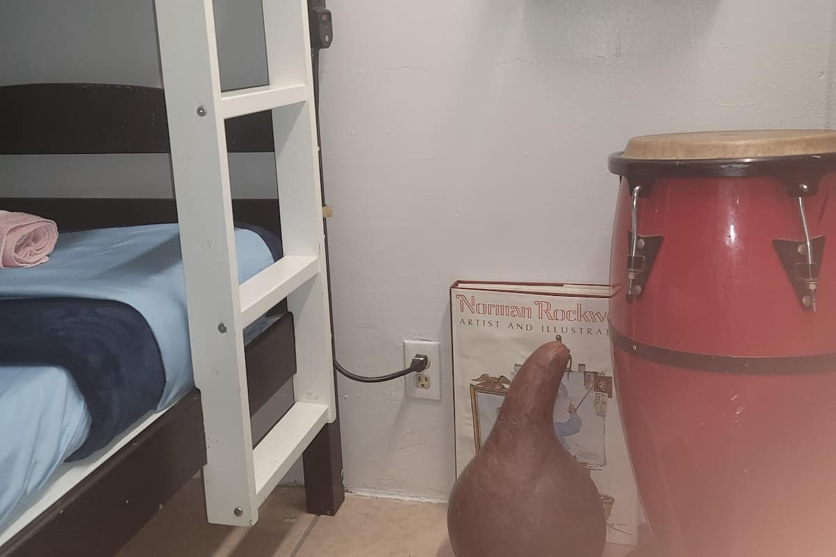A bunk bed with a blue mattress, a red drum, and a book titled "Norman Rockwell: Artist and Illustrator" on the floor.