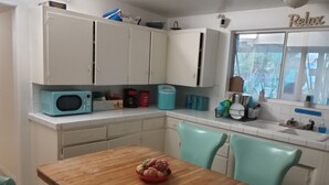 Une cuisine avec des meubles blancs, une table en bois et des chaises de couleur turquoise.