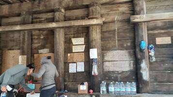 A rustic wooden cabin with a wooden ceiling and walls, a bench with water bottles, and a sign indicating a distance to Mexico.