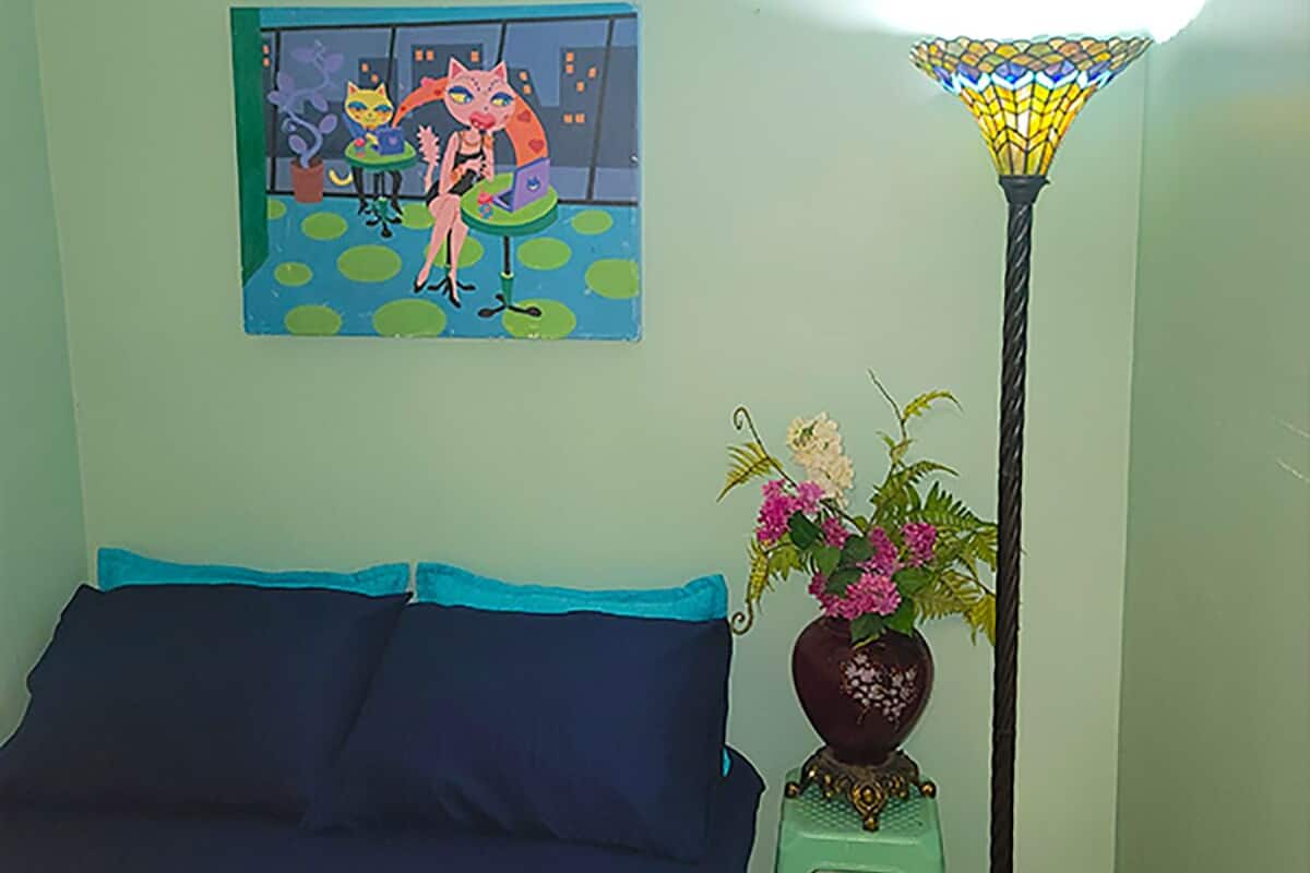 A room with a bed, a painting, a floor lamp, and a small table with a vase of flowers.