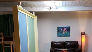 Un salon avec un canapé en cuir marron, une batterie rouge, un tableau accroché au mur et une échelle appuyée contre un mur.