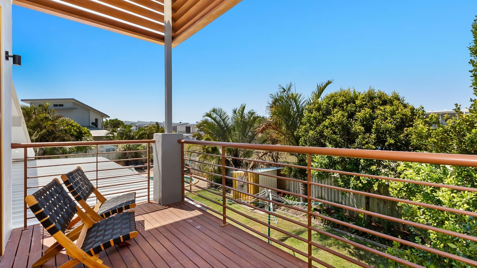 A wooden deck with two lounge chairs, a metal railing, and a view of a residential area with houses and greenery.