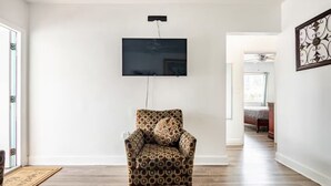 A spacious room with a patterned armchair, a flat-screen TV mounted on the wall, and a wooden floor.