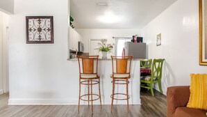 A compact living space with two bamboo chairs, a small kitchen area, and a sofa with a yellow cushion.