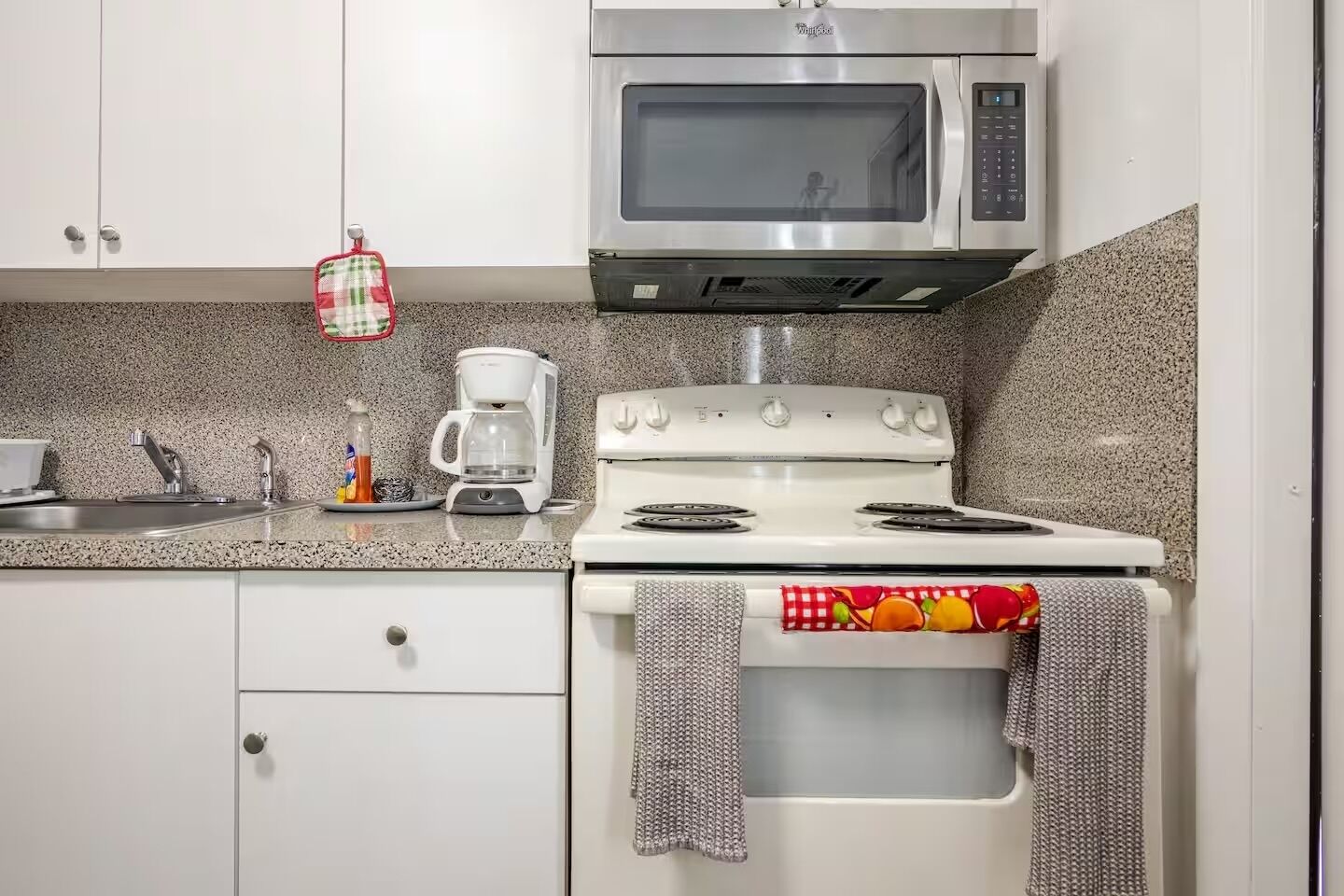 A kitchen with a microwave, stove, coffee maker, and a red and white checkered towel hanging on the oven door.