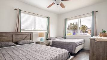 A bedroom with two beds, a ceiling fan, and a window with curtains.