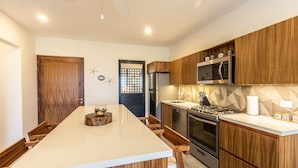Una cocina moderna con armarios de madera, una isla central, electrodomésticos de acero inoxidable y un elemento decorativo en la pared.
