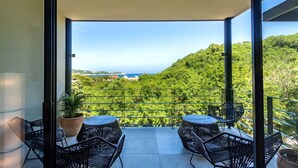 Un balcón con dos mesas redondas y cuatro sillas, con vistas a un paisaje verde exuberante y el mar.
