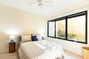 A bedroom with a bed, two bedside tables with lamps, a ceiling fan, and a large window with a view of a garden. - Modern condo w/ private terrace and plunge pool (Huatulco)