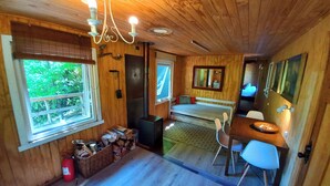 A cabin interior with a wooden ceiling, a bed, a dining table with chairs, a fireplace, and a window with a view of greenery. - Conguillio Park Cabin Cabin 3 people (Melipeuco)