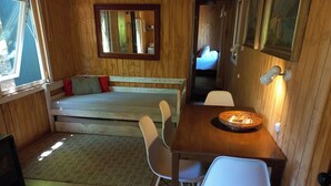 A cozy room with a wooden floor, a sofa with cushions, a dining table with chairs, and a mirror on the wall. - Conguillio Park Cabin Cabin 3 people (Melipeuco)