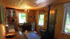 A cozy cabin interior with a dining area, kitchen, and wood stove. - Conguillio Park Cabin Cabin 3 people (Melipeuco)